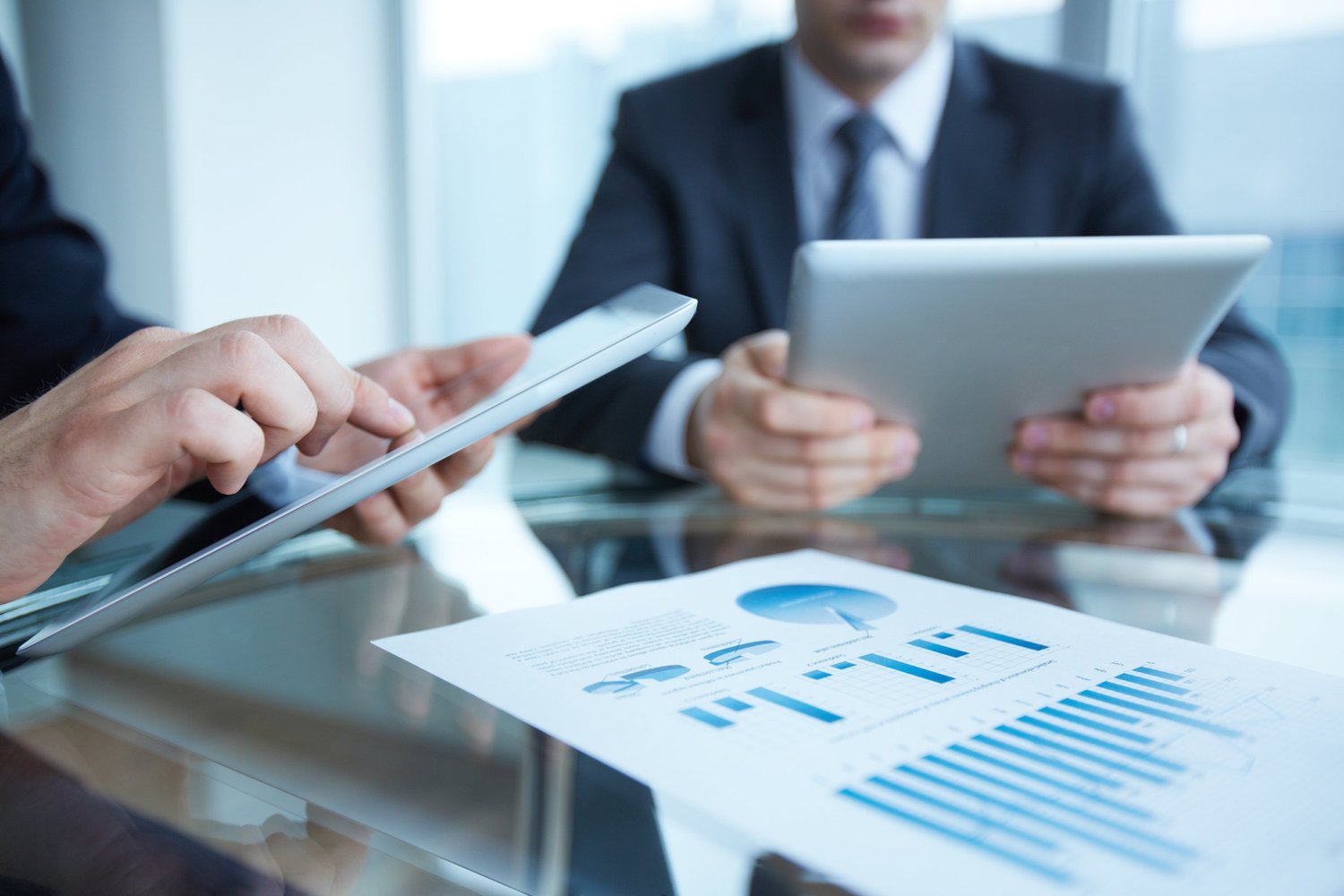 Business professionals in a meeting discussing financial charts with digital tablets and printed graphs.