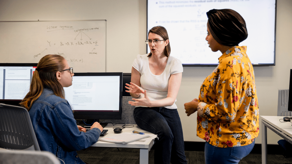 Three women engaged in a discussion in an office setting.